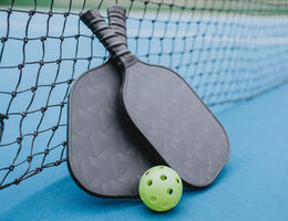 A pickleball between two rackets leaning against a pickleball net.
