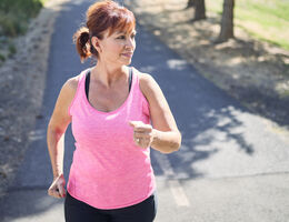 A woman speed walks on a paved trail.