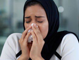A woman blows her nose into a tissue.