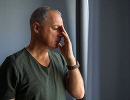 A man shuts his eyes and raises his hand to his face