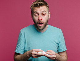 A man with a reddened nose holds a tissue and prepares to sneeze.