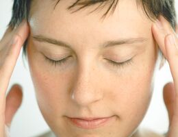 A woman touches her temple with her eyes closed.