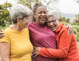 Three women laugh and embrace.