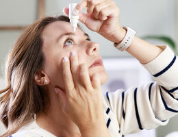 A woman putting eye drops in her eye.