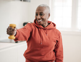 A smiling woman extends a hand weight.