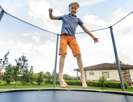 A boy bouncing on a backyard trampoline, surrounded by a mesh wall.