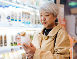  In the dairy aisle of a grocery store, a woman reads a milk bottle.