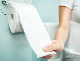 A hand pulls toilet paper from a roll.
