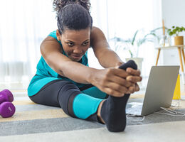 A woman stretches in front of a laptop.