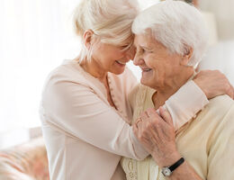 A woman hugs an older woman as they both smile.