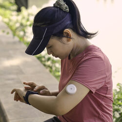 A woman with a CGM on her arm checks her smartwatch.