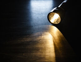 A lighted flashlight on a hardwood floor.