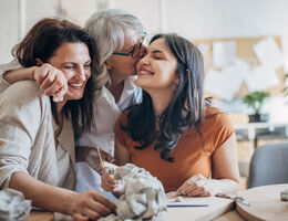 A grandmother hugs her daughter and young adult granddaughter.