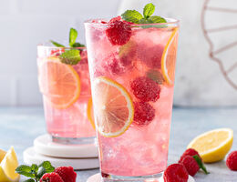 Two ice-cold glasses full of sparkling water, raspberries, lemon slices and mint leaves.