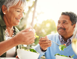 A smiling couple eating salad.