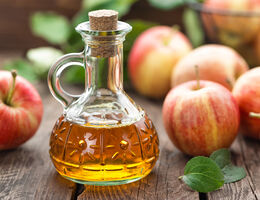 A corked carafe of apple cider vinegar surrounded by apples.
