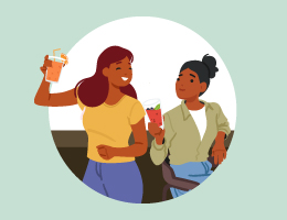 Two women at a bar raise their glasses of fruity drinks.