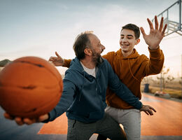 An older man plays basketball with a teen boy.