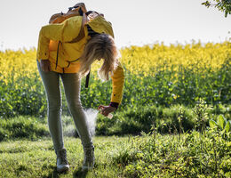 A woman in hiking clothes sprays bug repellent on her ankles.