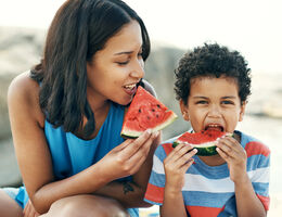 A woman and child each eating a slice of watermelon.