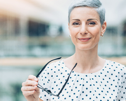 Older woman in hospital gown holding her glasses.