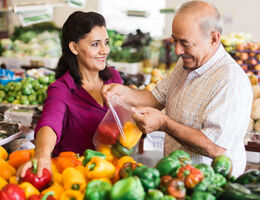 An older couple chooses bell peppers at a grocery store.
