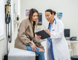 A young woman sits on an exam table talking to a doctor.
