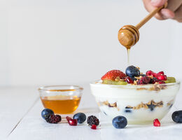 A bowl of yogurt topped with fresh fruit, granola and honey.