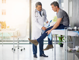 A man sits on an exam table as a doctor looks at his knee