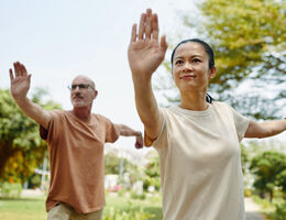 A woman and a man do tai chi outdoors.