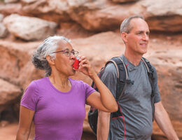 A woman uses her inhaler as she and a man hike.