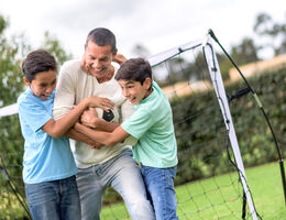 A man and two boys play with a soccer ball.