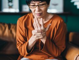 A woman sits on a couch, massaging her hand.