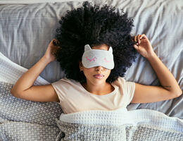 A woman in bed with a sleep mask over her eyes.