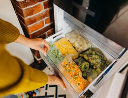 A person opening a freezer drawer full of bagged vegetables.