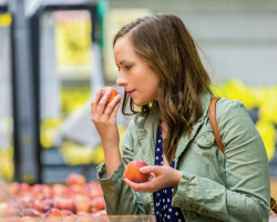 A woman smells a peach from a bin.