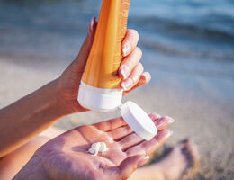 A person’s hand squeezes sunscreen from a tube into the palm of their other hand.