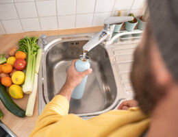 A man fills a water bottle at a kitchen sink.