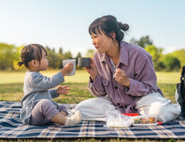  A woman and toddler on a picnic blanket, mugs raised