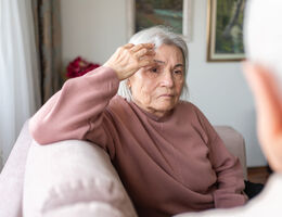 A woman with a drooping mouth on one side sits on a couch.