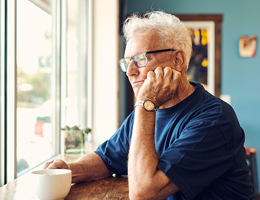 A man rests his hand on his chin near the window of a coffee shop. 