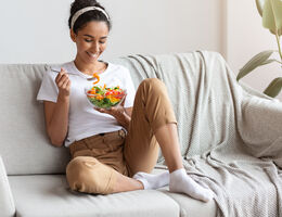 A woman on a couch smiles at her salad.