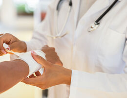 A doctor rolls gauze around a patient’s arm.