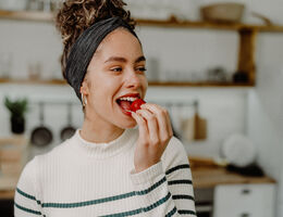 A smiling woman eats a strawberry.