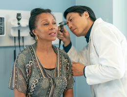 A doctor uses an otoscope to look in a woman's ear. 