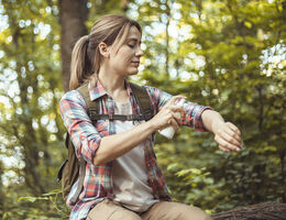 A woman on a hiking trail sprays mosquito repellent on her arm.