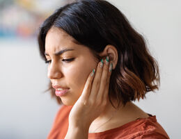 A woman frowns as she holds a hand to her ear.