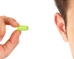 A hand holds a foam earplug near a man's ear.