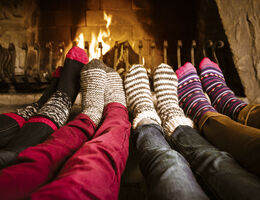 Four pairs of feet with winter socks rest cozily in front of a fireplace.