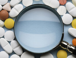 A magnifying glass surrounded by pills and capsules. 